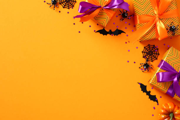 istock Happy Halloween holiday banner template with gift boxes, spiders, bats, confetti on orange background. Flat lay, top view, copy space. 1431624004