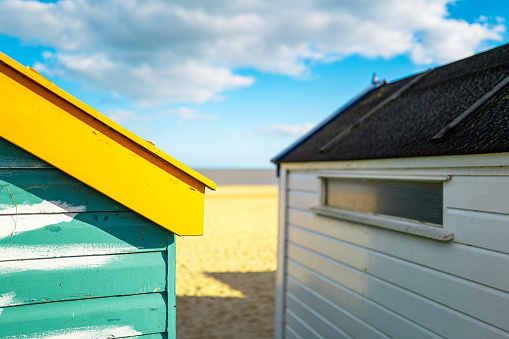 Shallow focus of a repaired, wooden beach hut showing wood filler being applied to the brightly painted wooden panels. A distance Suffolk beach and North Sea can be seen.