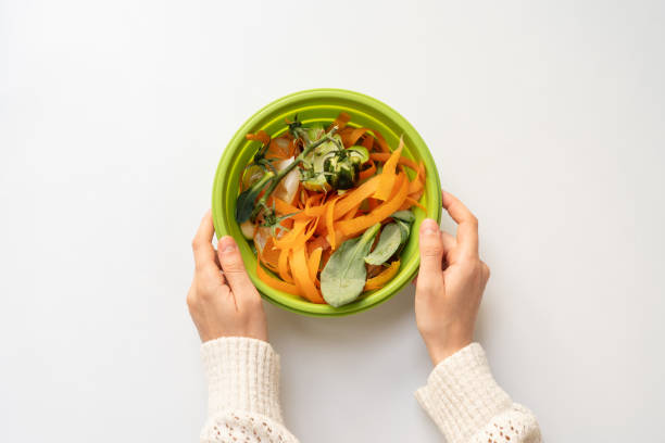 Woman holding a bowl with vegetable peelings Woman holding a bowl with vegetable peelings, concepts of avoiding food waste and waste sorting mezzaluna stock pictures, royalty-free photos & images