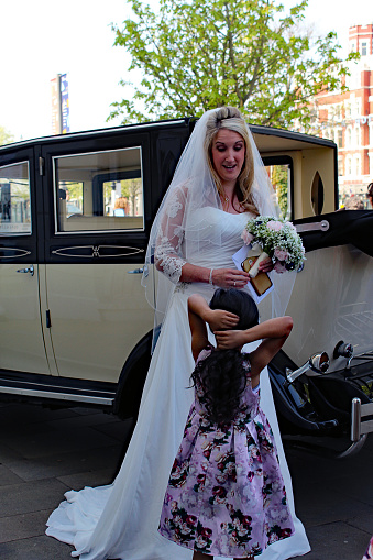 A bride talks to one of her flower girls on her wedding day. The bride is a Caucasian female, the flower girl is a black female. Both of these families are closed and shared this special celebration together.