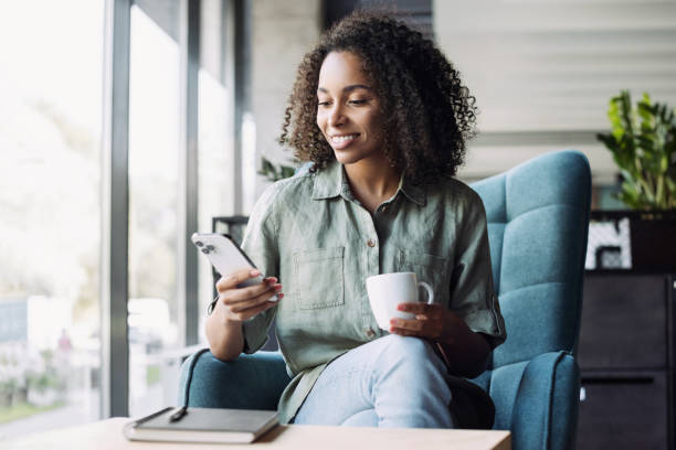Young woman using smartphone in office, has coffee break stock photo