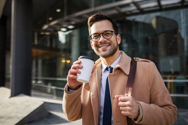 istock Handsome young businessman walking drinking coffee looking at camera 1431635331