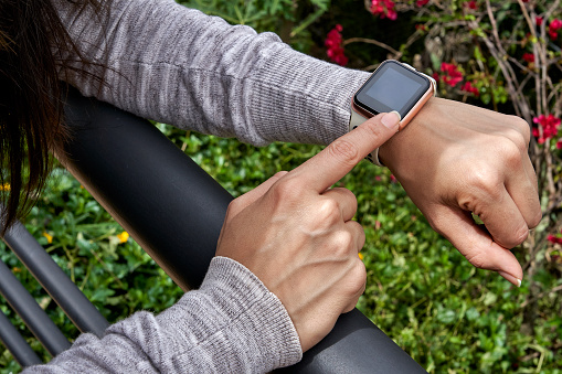 Young woman tries out a generic but modern touch screen smart-watch on his wrist. Using finger to tapping the home screen to make a phone call or send a text message