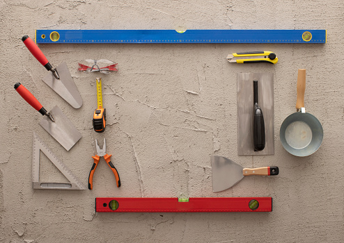 Various construction, DIY hand tools on a concrete background. Tools include: hammer, level, tape measure, masonry equipment, scalpel,  pliers and nippers