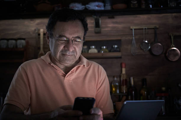 istock Senior Hispanic man using smart phone in a domestic kitchen home office with low lighting 1431636162