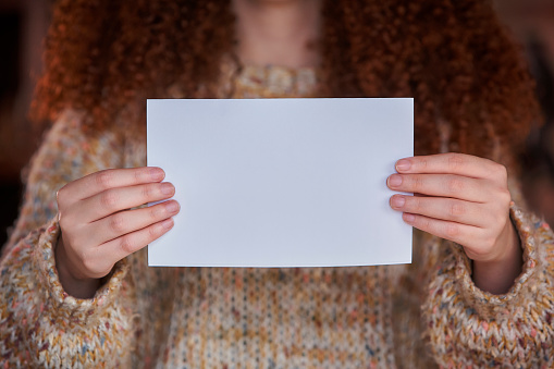 Close-up of curly red hair Irish young woman holding a white paper with copy space ready for text or advertisement.