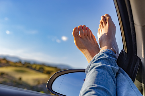 Madrid Spain. May 7, 2022. Tall legs with bare feet on car window. Rural image of sky, field and mountain in the background. Sunny day