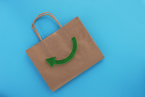 Cardboard paper bag with recycling symbol green arrow on light blue background