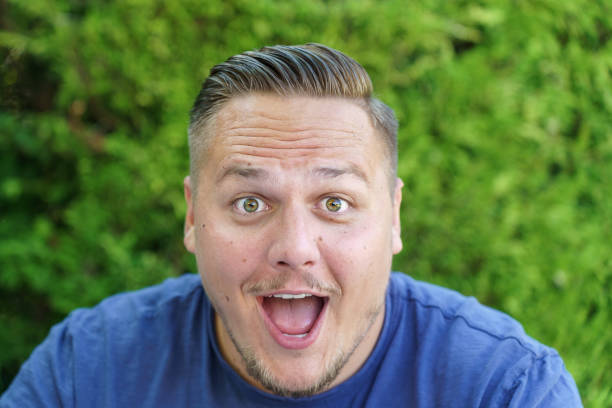 Young man gawping at the camera with mouth open and wide surprised eyes in close up outdoors in the garden