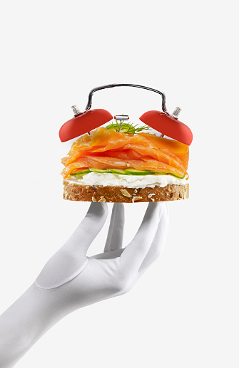 Gloved hand presenting salmon sandwich with with alarm clock bells