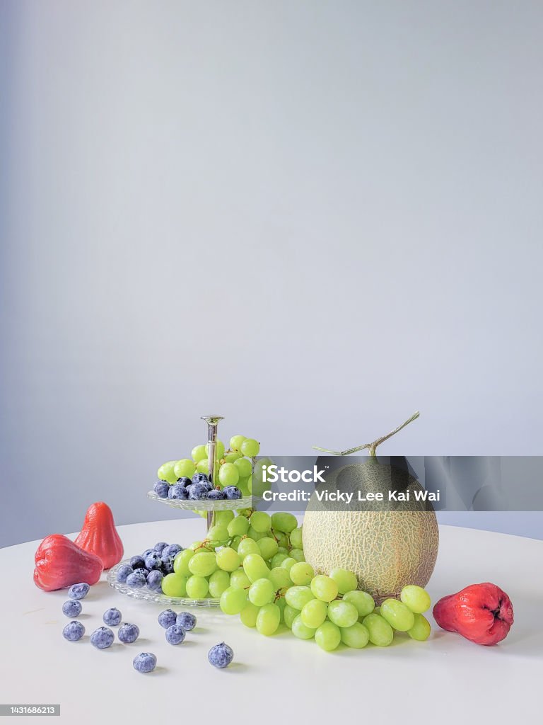Exhibición de frutas mixtas en mesa blanca contra pared azul - Foto de stock de Fruta libre de derechos Exhibición de frutas mixtas en mesa blanca contra pared azul - Foto de stock de Fruta libre de derechos