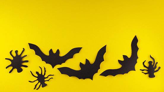 Halloween creative background with bats and spiders on yellow background. Halloween paper decorations. Top view. Copy space