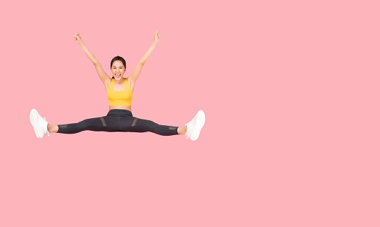 Full length body size Cheerful woman jumping to the air hands raised wearing sportswear with excited jump on pink background and copy space Health care Healthy Lifestyle Exercise and Workout concept