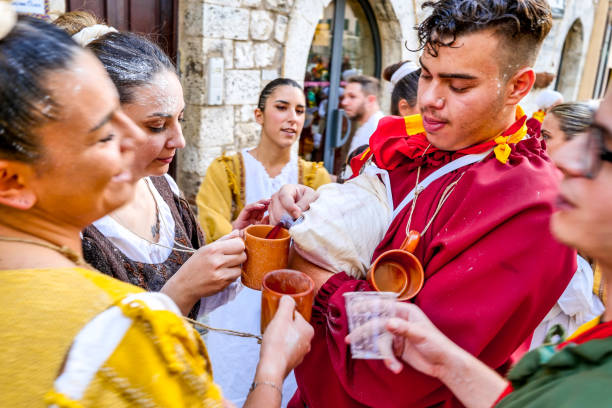 Young people in colorful period costumes celebrate and drink wine during the Palio in a medieval town of Umbria Gualdo Tadino, Umbria, Italy, September 30 -- A scene from the traditional Palio di San Michele Arcangelo (Palio of St Archangel Michael) in the medieval town of Gualdo Tadino, in Umbria. An ancient three-day festival that involves the entire community in a traditional Corteo Storico (Historical and Allegoric Parade) and culminates with a donkey race between the four 'contrade' (districts) of this medieval town. In the photo, some young people in a beautiful and colorful medieval costume celebrate and drink wine during the Historical and Allegoric Parade. An important center since Roman times, Gualdo Tadino rises between Foligno and Gubbio along the ancient Flaminia consular road, traced by the Romans. Its history spans the entire Middle Ages and, despite being partially destroyed and sacked several times and placed under the dominion of Perugia, this ancient Umbrian center still retains its medieval charm. The Umbria region, considered the green lung of Italy for its wooded mountains, is characterized by a perfect integration between nature and the presence of man, in a context of environmental sustainability and healthy life. In addition to its immense artistic and historical heritage, Umbria is famous for its food and wine production and for the high quality of the olive oil produced in these lands. Image in high definition format. gualdo tadino stock pictures, royalty-free photos & images