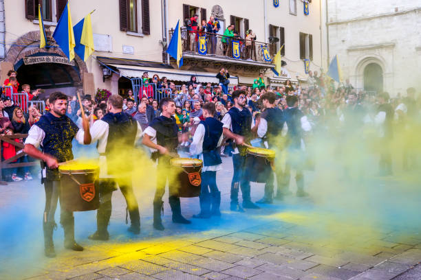 A colorful performance of drummers in period costume during a Palio in a medieval village in Umbria Gualdo Tadino, Umbria, Italy, October 01 -- A scene from the traditional Palio di San Michele Arcangelo (Palio of St Archangel Michael) in the medieval town of Gualdo Tadino, in Umbria. An ancient three-day festival that involves the entire community in a traditional Corteo Storico (Historical and Allegoric Parade) and culminates with a donkey race between the four 'contrade' (districts) of this medieval town. In the photo, a group of young drummers perform in medieval costume in a very colorful scene during the Historical and Allegoric Parade in the town square. An important center since Roman times, Gualdo Tadino rises between Foligno and Gubbio along the ancient Flaminia consular road, traced by the Romans. Its history spans the entire Middle Ages and, despite being partially destroyed and sacked several times and placed under the dominion of Perugia, this ancient Umbrian center still retains its medieval charm. The Umbria region, considered the green lung of Italy for its wooded mountains, is characterized by a perfect integration between nature and the presence of man, in a context of environmental sustainability and healthy life. In addition to its immense artistic and historical heritage, Umbria is famous for its food and wine production and for the high quality of the olive oil produced in these lands. Wide angle image in high definition format. gualdo tadino stock pictures, royalty-free photos & images