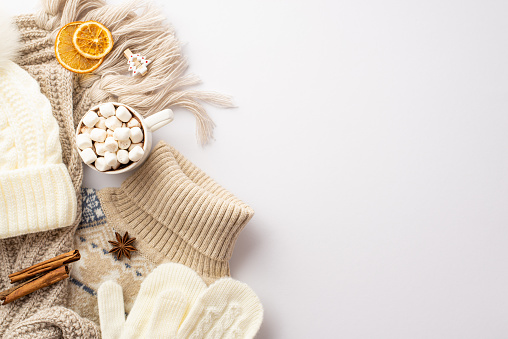 Winter concept. Top view photo of sweater scarf hat mittens cup of cocoa with marshmallow decorative wooden clip dried orange slices anise cinnamon sticks on isolated white background with copyspace
