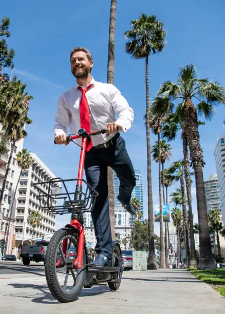 Happy man in formalwear ride e-scooter on sidewalk, e-scooting.