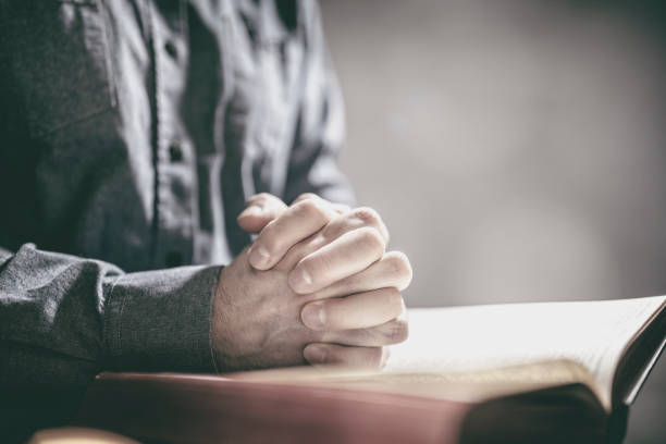 Hands folded in prayer on a Holy Bible in church background, faith, spirtuality and religion Hands folded in prayer on a Holy Bible in church background concept for faith, spirtuality and religion new testament stock pictures, royalty-free photos & images
