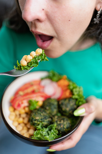 Woman eating vegan food bowl full of vegetables. Close up caption. Vertical photography