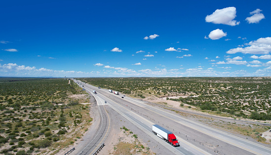 Red and Blue semi-trucks driving on a interstate 10 in Texas, USA - aerial view