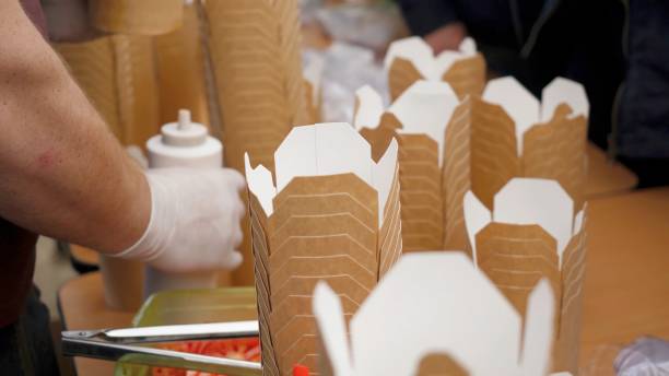 mani che mettono il contenitore per alimenti da a portata di mano, da vicino. consegna di cibo. primo piatto dello chef che serve una singola porzione di noodles fritti saltati in padella cinese nella scatola da a portata di cibo cinese - pizza box foto e immagini stock