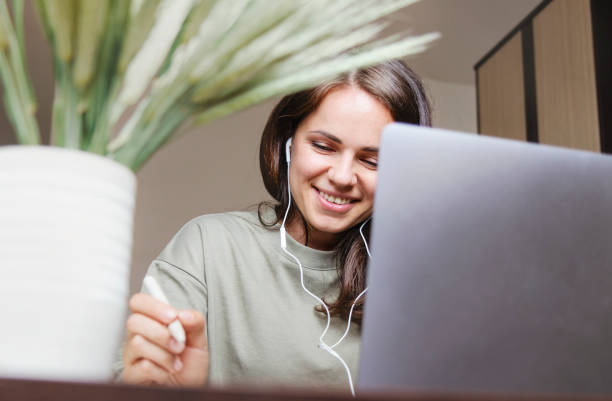 femme aux cheveux bruns travaillant à domicile participant à un appel vidéo à l’aide de son ordinateur portable. - women computer home interior brown hair photos et images de collection