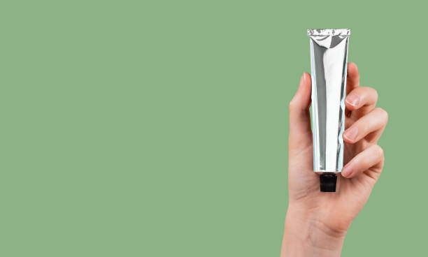 hand holding silver aluminum cream tube mock up on eco green background, ad banner with copy space for text - moisturizer cosmetics merchandise human hand imagens e fotografias de stock