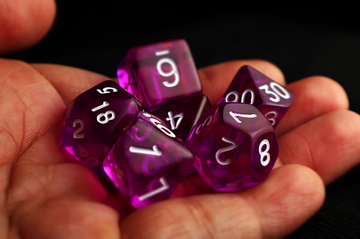 a hand holding purple role playing dices with various shapes with dark background