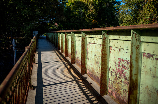 Views of a bridge in suburban Wellesley, MA that spans over the commuter rail tracks.  Photos show the rusty metal structure from various angles. This bridge is heavily used by morning commuters, joggers and cyclists and leads directly to the Wellesley Hills MBTA commuter rail station.