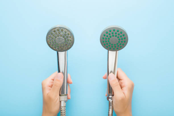 Woman hands holding new and old shower heads on light blue table background. Pastel color. Compare two objects with and without limescale. Dirty and clean. Closeup. Point of view shot. Top down view. stock photo
