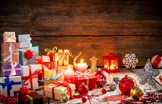 Many gift boxes stacked in Christmas on wooden background with christmas lights and candle lantern