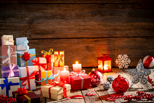 Many gift boxes stacked in Christmas on wooden background with christmas lights and candle lantern