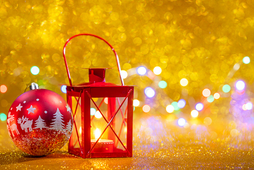 Red candle lantern in golden glitter Christmas background and red bauble with blurred Christmas lights bokeh