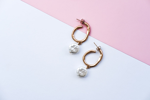 Gold earrings with white pearls on a white-pink paper background. Flat lay, place for text.