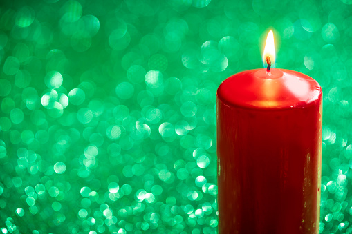 A burning pillar candle with decoration stands against a background with blurred light spots