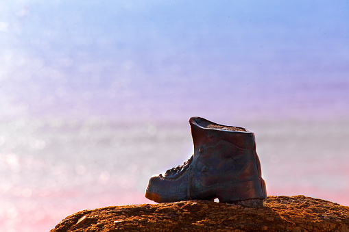 Finisterre Cape viewpoint at sunset with  cast bronze hiker boot . Pilgrimage   boot at the end of camino de santiago.