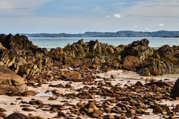 Rocky coastline with mountains emerging from the sea in the background on a cloudy day