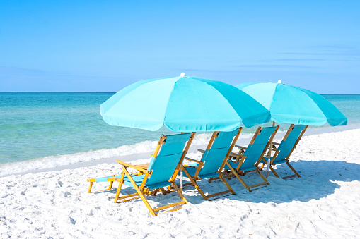 A group of blue beach chairs with umbrellas sitting on white sandy beaches in front of the ocean.
