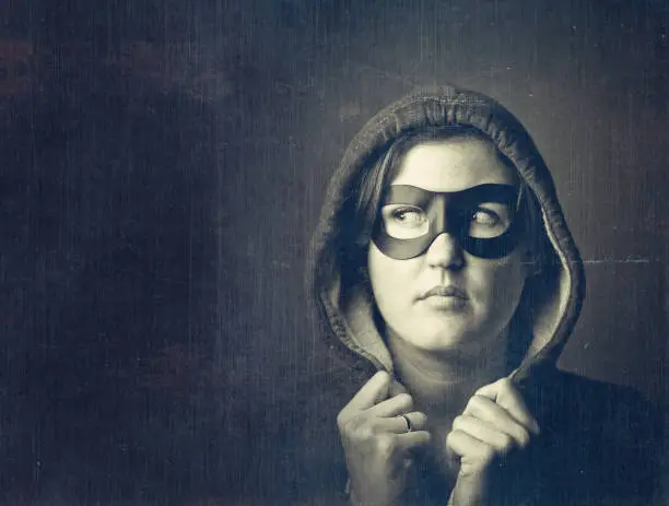 woman with a black mask and a hood wear, looking away from camera, grunge textures overlay