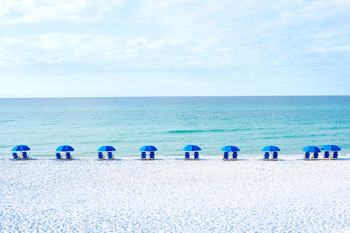 A row of blue beach chairs with umbrellas sitting on white sandy beaches in front of the ocean.
