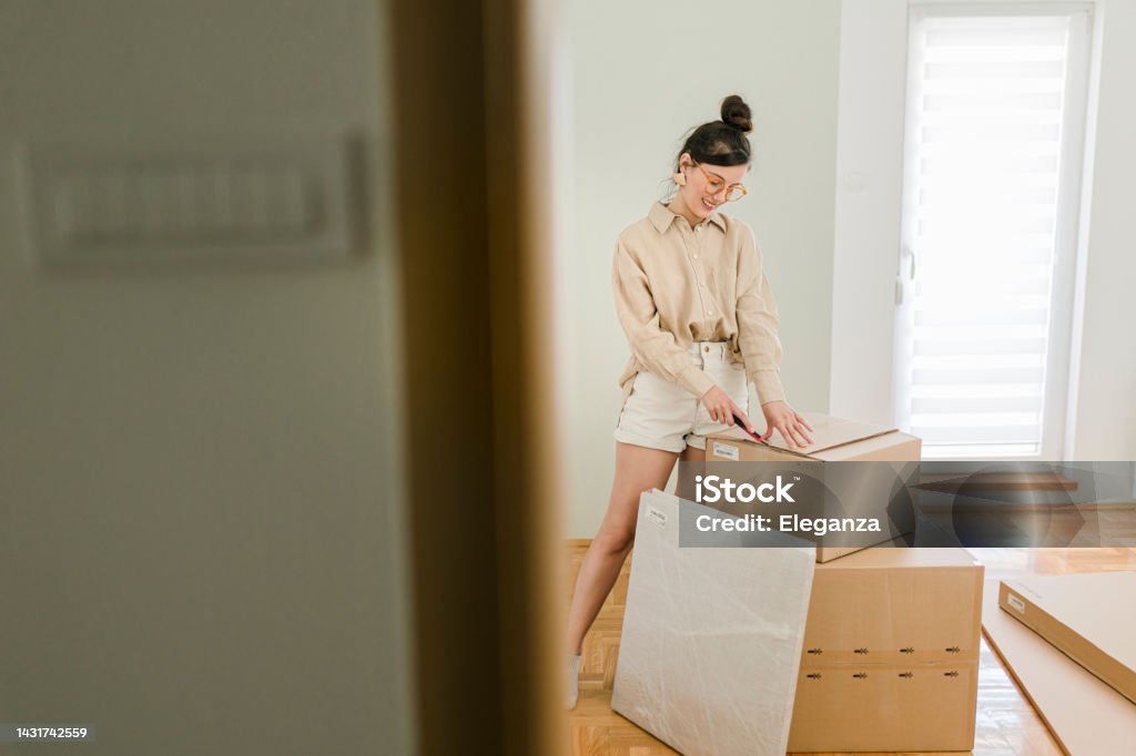 Portrait of a happy  young woman unpacking her belongings while moving in Adult Stock Photo