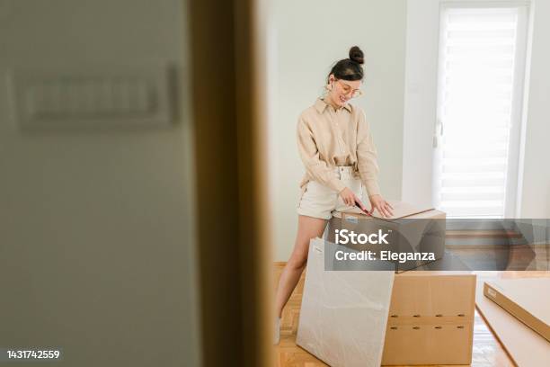 Portrait Of A Happy Young Woman Unpacking Her Belongings While Moving In Stock Photo - Download Image Now