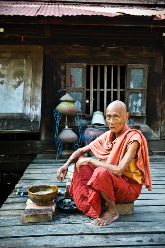 A Burmese monk in his 70s, sitting outside his monastery where he is washing dishes, in Mandalay, Myanmar
