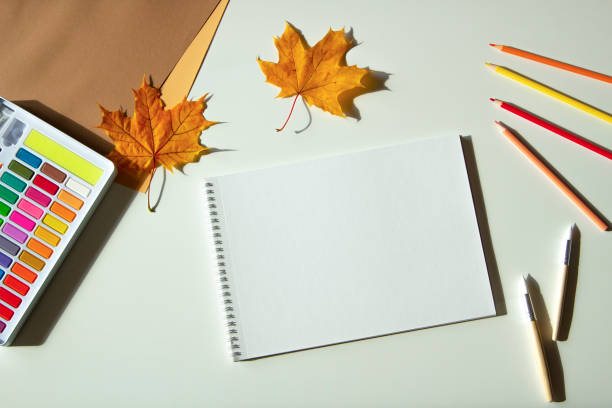 istock Autumn composition. Watercolor paint and brushes, open blank spirale sketchbook, colored pencils and autumn maple fall leaves on white desk background. Top view, copy space for text 1431746637