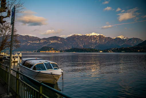 Boat next to shore and idyllic  landscape with lake como and snow-capped mountains (italian Alps or South Alps) On other side of lake - Belaggio or San-Giovanni.