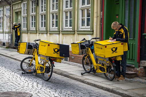 German postman of the Deutsche Post delivering mail using an electric bicycle. Werningrode, Germany - April 26, 2018