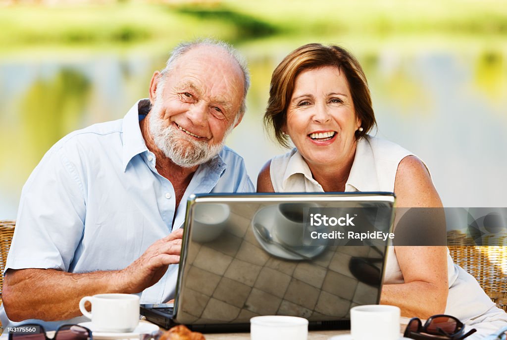 Souriant mature couple partage un ordinateur portable sur la terrasse au bord du lac - Photo de Adulte libre de droits