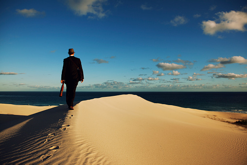 A male businessman walks through the desert to the sea to find more business. 