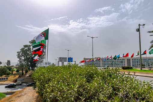 Dar El Beida, Algiers - October 8, 2022: Flags of Arab countries and Hyatt Regency hotel near the airport with road sign panels. Arab League Summit in November 2022. Trees, cars and cloudy sky.