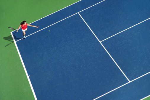A yellow tennis ball and tennis racket lies on the clay court.